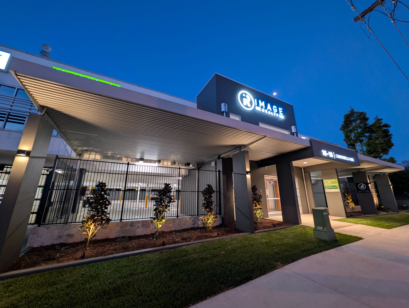 Commercial building exterior at dusk with column wall lights, soffit lighting and garden uplights, South East Queensland